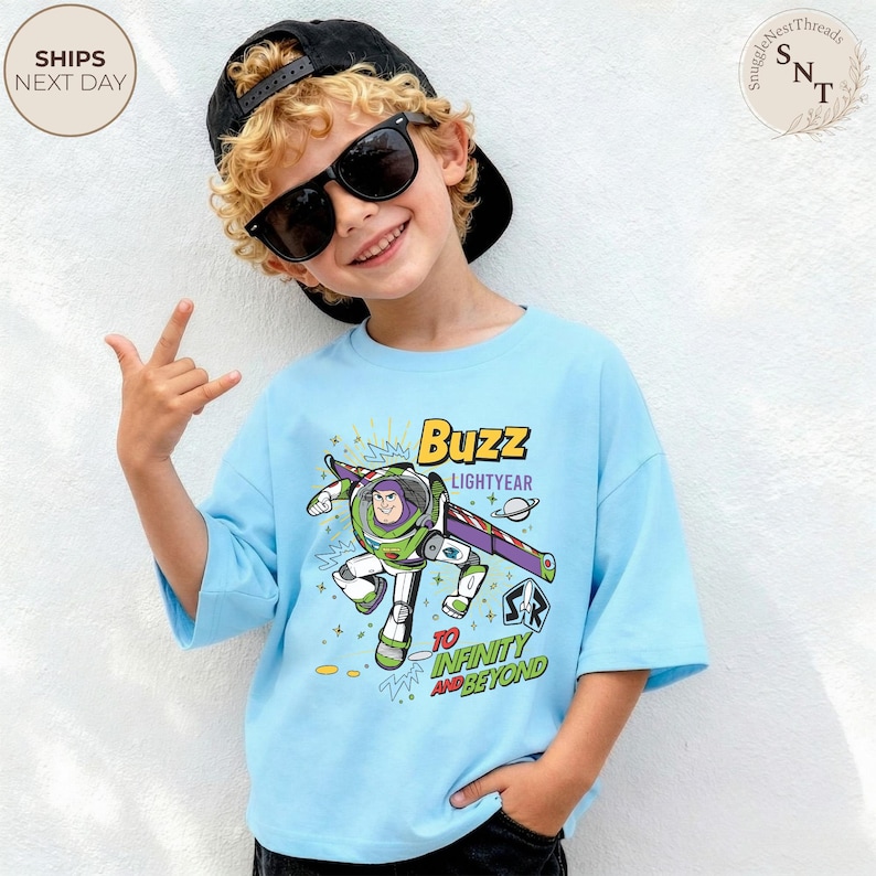 Puede incluir: Camiseta azul claro de Buzz Lightyear con un gr&aacute;fico del personaje en su traje espacial, las palabras "Buzz Lightyear" y "To Infinity and Beyond". La camiseta tiene mangas cortas y un corte holgado.
