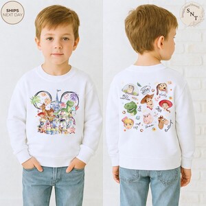 Puede incluir: Una sudadera blanca de manga larga con un gr&aacute;fico frontal de varios personajes animados dispuestos en forma de orejas de Mickey Mouse y un gr&aacute;fico trasero con caras de personajes y nombres como Buzz Lightyear, Woody y Jessie.