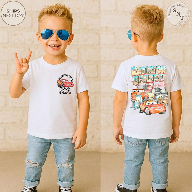 May include: White t-shirt featuring a cartoon car design with the name "David" printed below. The back of the shirt displays "Radiator Springs" with various car characters. The child is wearing blue sunglasses and ripped jeans.