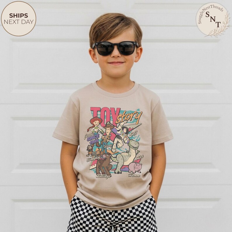 Puede incluir: Una camiseta de manga corta de color beige con un estampado gr&aacute;fico colorido de los personajes de Toy Story, incluyendo a Woody, Buzz Lightyear, Jessie, Slinky Dog, Bullseye, Rex y Hamm, con el texto Toy Story y los nombres impresos.