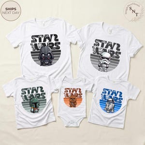 May include: White t-shirts and a onesie featuring Star Wars characters: Darth Vader, Stormtrooper, Boba Fett, Chewbacca, and R2-D2. Each shirt has a character graphic within a gray and white striped circle, with "STAR WARS" text above.