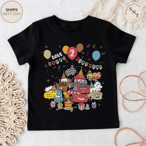 Puede incluir: Camiseta negra con un estampado colorido de coches de dibujos animados, globos y elementos de cumplea&ntilde;os. Incluye el texto "DAVE HAPPY BIRTHDAY 2". La imagen presenta una tarta de cumplea&ntilde;os y regalos, ideal para el segundo cumplea&ntilde;os de un ni&ntilde;o.