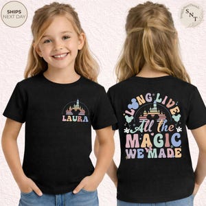 May include: Black t-shirt featuring a colorful castle design with the name "LAURA" on the front. The back of the shirt displays the text "LONG LIVE All the MAGIC WE MADE" in pastel colors. A children's apparel item.