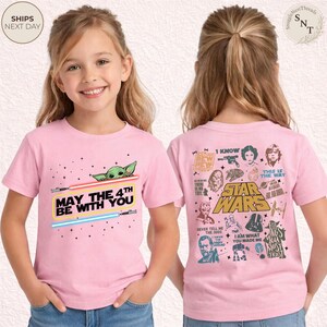 May include: Pink t-shirt featuring a graphic of Baby Yoda, lightsabers, and the text "May the 4th Be With You." The back of the shirt has Star Wars characters and quotes. A fun, themed tee.