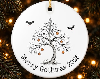 May include: A round white ceramic ornament featuring a black ink illustration of a bare tree decorated with small orange spheres and white skulls. Two black bats fly above the tree. The text Merry Gothmas 2026 is printed in black.