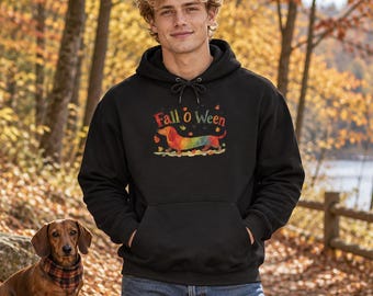 May include: A black hooded sweatshirt featuring a graphic of a dachshund with a rainbow-colored coat, surrounded by autumn leaves and the text Fall o ween. The hoodie includes a front kangaroo pocket and black drawstring cords.