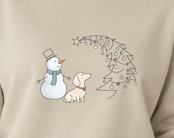 May include: A beige crewneck sweatshirt featuring a line art graphic of a snowman with a blue scarf, a light-colored dachshund, and a stylized Christmas tree decorated with small ornaments, bells, and a star at the top of the tree.
