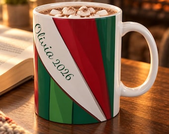 May include: A white ceramic mug filled with a hot beverage topped with marshmallows. The mug features a diagonal design of red and green stripes and the text Olivia 2026 printed in dark green script on a white background.