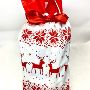 May include: A white gift bag with a red and white Scandinavian pattern featuring reindeer and snowflakes. The bag is tied with a red ribbon.