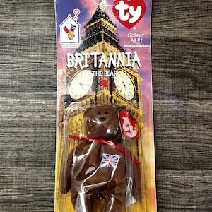 May include: A brown plush bear toy named "Britannia" with a Union Jack flag on its chest, packaged on a card featuring Big Ben. The bear has a red ribbon and a "Ty" heart tag.