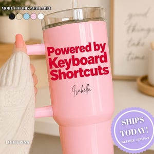 May include: A light pink insulated tumbler with a handle and a clear lid. The tumbler features the red text Powered by Keyboard Shortcuts and the name Isabella in black script. A row of five colored circles indicates more colors are available.