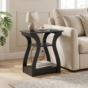 May include: A black end table with a rectangular top, a middle shelf, and a bottom shelf. The table features curved side supports and a built-in power outlet on the middle shelf. A beige lamp sits on the top surface, and books are on the bottom shelf.