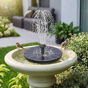 Op de afbeelding: Een fontein op zonne-energie in een stenen vogelbad. De fontein spuit water omhoog en cre&euml;ert een kleine waterpartij. Twee kleine vogels zitten op de rand van het vogelbad, dicht bij het water.