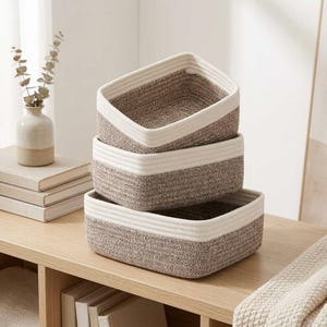 May include: A set of three rectangular storage baskets stacked vertically. Each basket is constructed from coiled rope with a two-tone design featuring a dark brown speckled base and a solid cream-colored top rim, creating a structured storage solution.