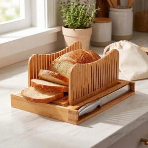 May include: A bamboo bread slicer guide with vertical slots for consistent cutting. The wooden unit holds a loaf of bread with three pre-cut slices resting in front. A serrated stainless steel bread knife is stored in a side compartment.