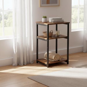 May include: A three-tiered side table with a rustic, industrial design. The table features a dark metal frame and shelves with a wood-grain finish. A rolled blanket, books, a small plant, and a candle are displayed on the shelves.