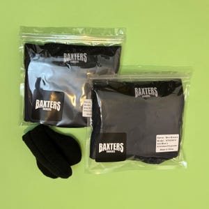 May include: Two pairs of dark blue boxers in clear plastic bags with Baxters Boxers branding and labels. Each bag features a black square logo with white text. A pair of black textured fabric items sits to the left of the packaged boxers.
