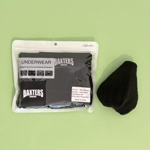 以下が含まれることがあります： 透明なビニール袋に入った黒いボクサーパンツ。袋には「Baxters Boxers」の文字と、「Name: Men Boxers, Model: NT650914, Size: Black-M, 95% Cotton/5% spandex, Made in China」と書かれたラベルがあります。袋の横には黒いふわふわした布製の物体が置かれています。