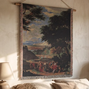 May include: A rectangular woven wall tapestry featuring a landscape scene with dark green trees, a distant mountain range, and figures in the foreground. The tapestry is suspended from a wooden rod with a rope and has frayed edges on the sides.