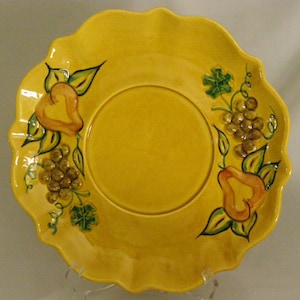 May include: A yellow ceramic serving dish with a scalloped edge. The dish is decorated with hand-painted pears and grapes in shades of green, yellow, and orange.