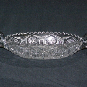 May include: A clear glass serving dish with two handles. The dish has a cut glass design with a starburst pattern.
