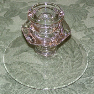 Puede incluir: Un candelero de vidrio transparente con una base redonda y un diseño acanalado. El candelero está sobre un mantel verde.