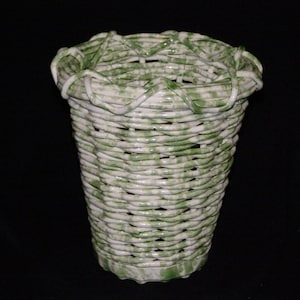 May include: A white ceramic vase with a green and white woven pattern. The vase is tall and narrow with a wide opening at the top.