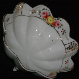 May include: A white porcelain bowl with a scalloped edge and a floral design in shades of pink, yellow, and green. The bowl has a gold trim and a raised center.