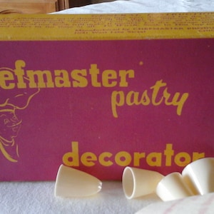 May include: A yellow and pink box with the text "Chefmaster pastry decorator" on the front. The box contains a set of white plastic piping tips.