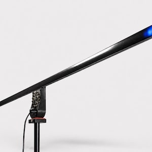 Peut inclure: Un luminaire rectangulaire noir avec une lumière bleue à l'extrémité. La lumière est montée sur un pied noir avec une base complexe et un cordon d'alimentation. Le fond est blanc uni.