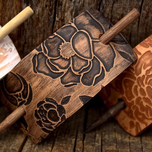 Puede incluir: Tres palos de pelo de madera con dise&ntilde;os florales tallados en la madera. Los palos son marrones y tienen un acabado natural. Las flores son negras y blancas.