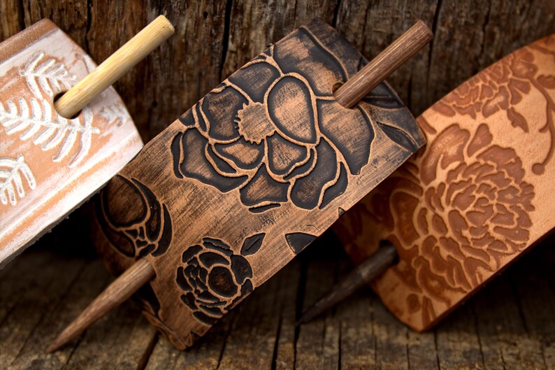 Puede incluir: Tres palos de pelo de madera con dise&ntilde;os florales tallados en la madera. Los palos son marrones y tienen un acabado natural. Las flores son negras y blancas.