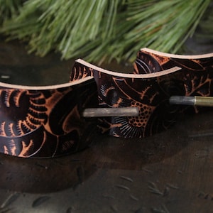Puede incluir: Tres horquillas para el pelo de cuero marr&oacute;n oscuro con intrincados dise&ntilde;os florales y palos de madera. Las horquillas son curvas y tienen un aspecto natural y artesanal, perfectas para a&ntilde;adir un toque r&uacute;stico a cualquier peinado.