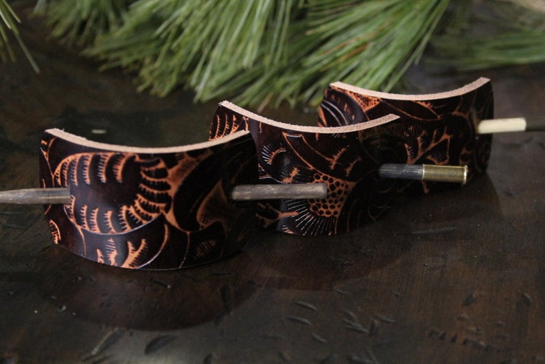 Puede incluir: Tres horquillas para el pelo de cuero marr&oacute;n oscuro con intrincados dise&ntilde;os florales y palos de madera. Las horquillas son curvas y tienen un aspecto natural y artesanal, perfectas para a&ntilde;adir un toque r&uacute;stico a cualquier peinado.
