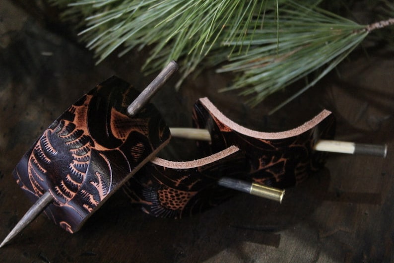 Puede incluir: Tres horquillas artesanales de cuero con intrincados dise&ntilde;os florales. El cuero marr&oacute;n oscuro se acent&uacute;a con detalles en marr&oacute;n claro. Cada horquilla presenta un pasador de metal para asegurar el cabello. Un accesorio natural y r&uacute;stico.