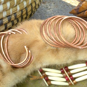 May include: Two sets of copper bangles, one set of five and one set of three, on a brown fur background.