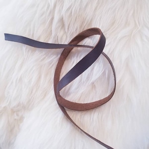 May include: A brown leather strap, coiled on a white fluffy surface.