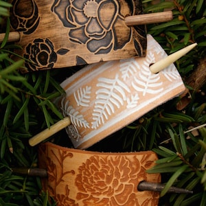 Puede incluir: Tres palos para el pelo de cuero con dise&ntilde;os florales. Los palos son marrones, blancos y naranjas con diferentes patrones florales. Cada palo tiene una clavija de madera.