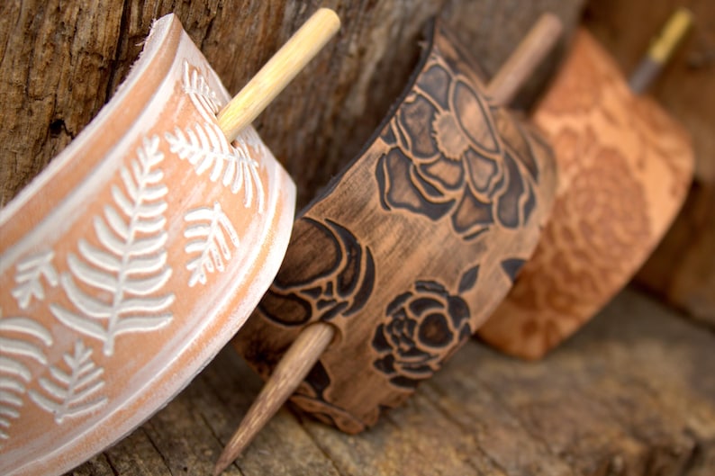 Puede incluir: Tres palos de pelo de madera con dise&ntilde;os decorativos. Los palos son marrones y tienen un acabado natural. Los dise&ntilde;os est&aacute;n tallados en la madera e incluyen helechos, rosas y un patr&oacute;n floral. Los palos miden aproximadamente 25 cm de largo.