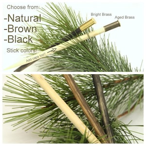 Puede incluir: Tres clavijas de madera con diferentes acabados: natural, marr&oacute;n y negro. Las clavijas se muestran con tapas de lat&oacute;n, una con un acabado brillante y la otra con un acabado envejecido. Las clavijas se muestran sobre un fondo de ramas de pino verdes.