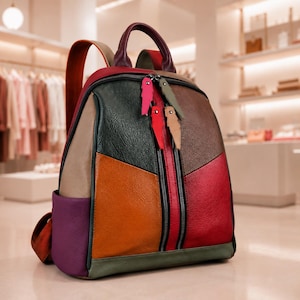 May include: A multi-colored backpack featuring a patchwork design of dark green, orange, red, brown, purple, and tan leather-like panels. It includes a top handle, two shoulder straps, and two front vertical zippered pockets with feather-shaped pulls.
