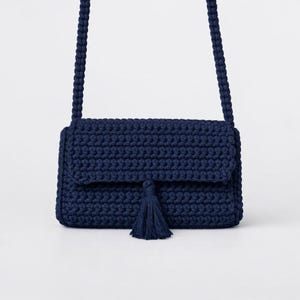 May include: A navy blue crochet crossbody bag with a flap closure and a tassel. The bag has a woven strap and is made of a thick, textured yarn. The bag is a stylish accessory.