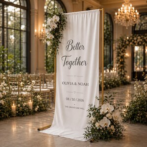 May include: A white fabric wedding sign with gold frame, adorned with floral arrangements. The sign reads "Better Together" with the names Olivia & Noah and the date 08/30/2026. The Grand Oak Hall is also listed.