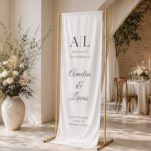 May include: A white wedding welcome sign with gold metal frame. The sign displays the initials "AL", followed by "Welcome to the wedding of Amelia & Lucas". The location and date are also printed on the sign: Rosewood Garden, Austin, TX, September 21, 2026.