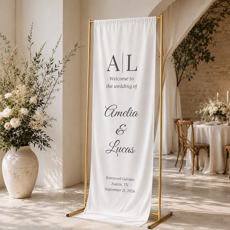 May include: A white wedding welcome sign with gold metal frame. The sign displays the initials "AL", followed by "Welcome to the wedding of Amelia & Lucas". The location and date are also printed on the sign: Rosewood Garden, Austin, TX, September 21, 2026.