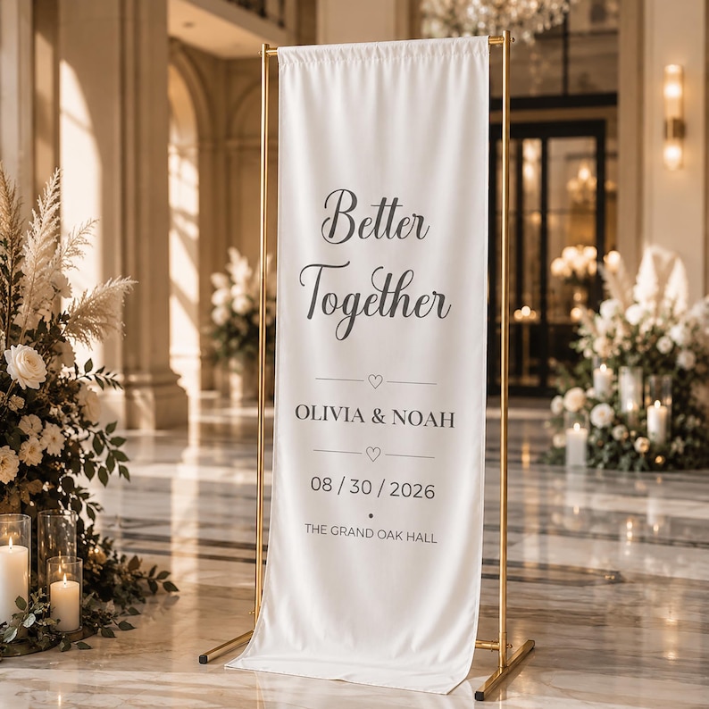 May include: A white fabric banner with the words "Better Together" in elegant script. Below, it reads "Olivia & Noah" and the date "08/30/2026". The banner is held by a gold metal stand, suitable for a wedding or event.