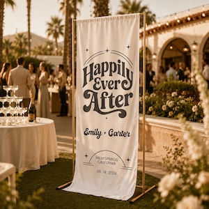 May include: A white banner with the words "Happily Ever After" in a retro font, with the names "Emily + Carter" and the date "06.14.2026" below. The banner is displayed on a gold metal stand at an outdoor wedding.
