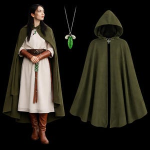 May include: An olive green hooded cloak with a clasp closure, displayed next to a person wearing a similar cloak and a white dress. The person is also wearing brown leather arm cuffs, a belt, and boots. A green leaf pendant hangs from a silver chain.