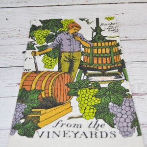 May include: A white rectangular kitchen towel with a vintage illustration of a man in a vineyard. The design includes barrels, grape vines, and the text "from the VINEYARDS". The color palette includes green, purple, orange, and yellow.