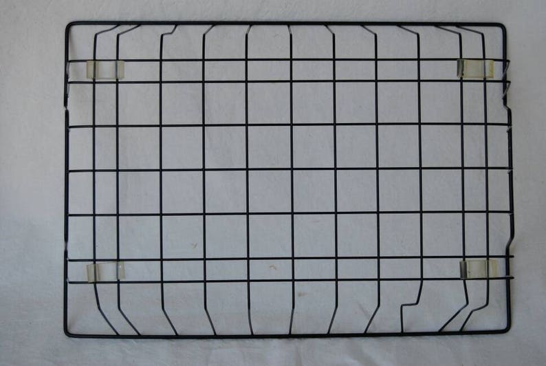 May include: A rectangular black metal grid with a square pattern, secured with clear plastic clips. The grid is designed for wall hanging. The background is a white fabric.